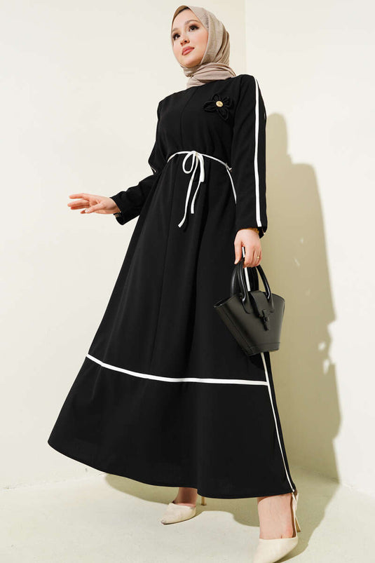 Schwarzes Kleid mit floralem Accessoire und Paspelierung