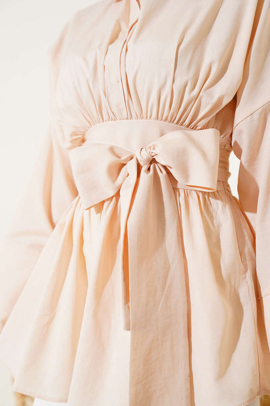 Tunique beige à ceinture intégrée et froncée sur le devant.