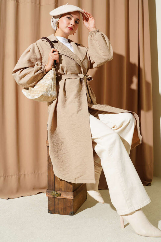 Trench-coat beige à double boutonnage, manches bouffantes et ceinture.