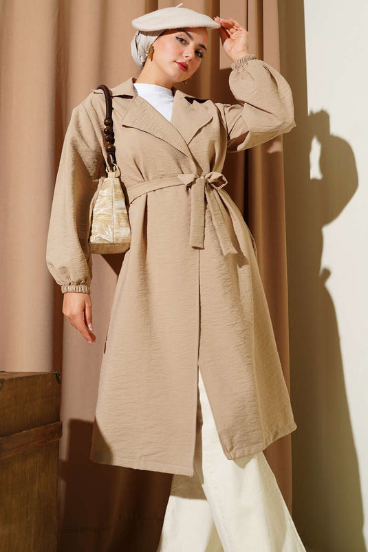 Trench-coat beige à double boutonnage, manches bouffantes et ceinture.