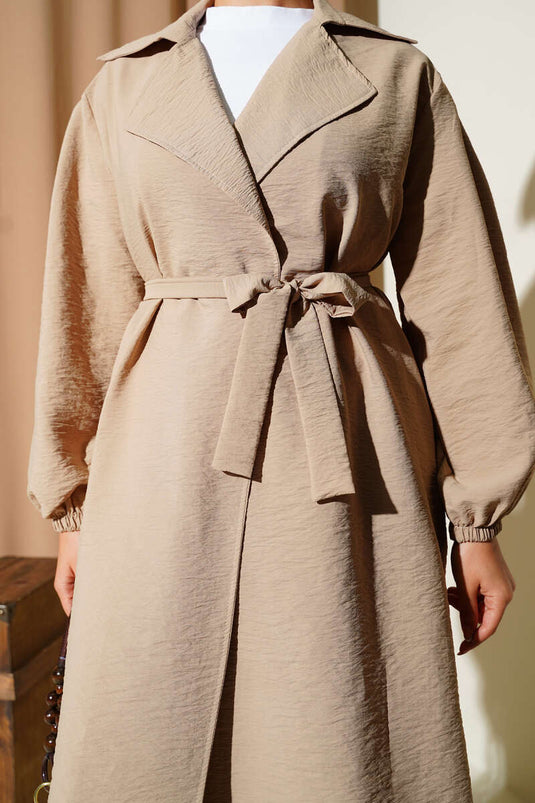 Trench-coat beige à double boutonnage, manches bouffantes et ceinture.