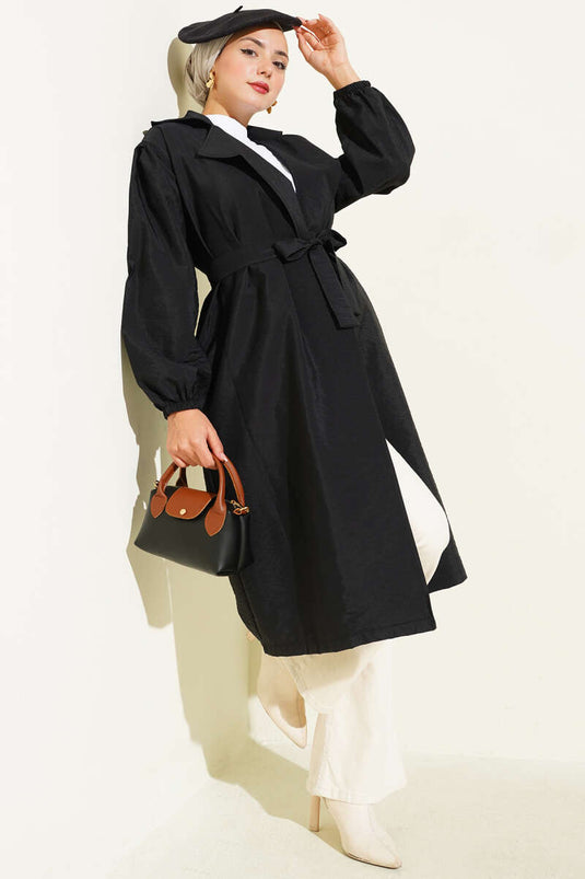 Trench-coat noir à double boutonnage, manches bouffantes et ceinture.