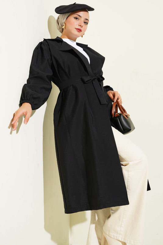 Trench-coat noir à double boutonnage, manches bouffantes et ceinture.