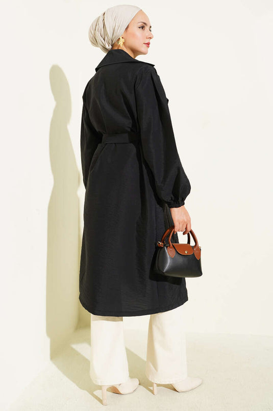 Trench-coat noir à double boutonnage, manches bouffantes et ceinture.