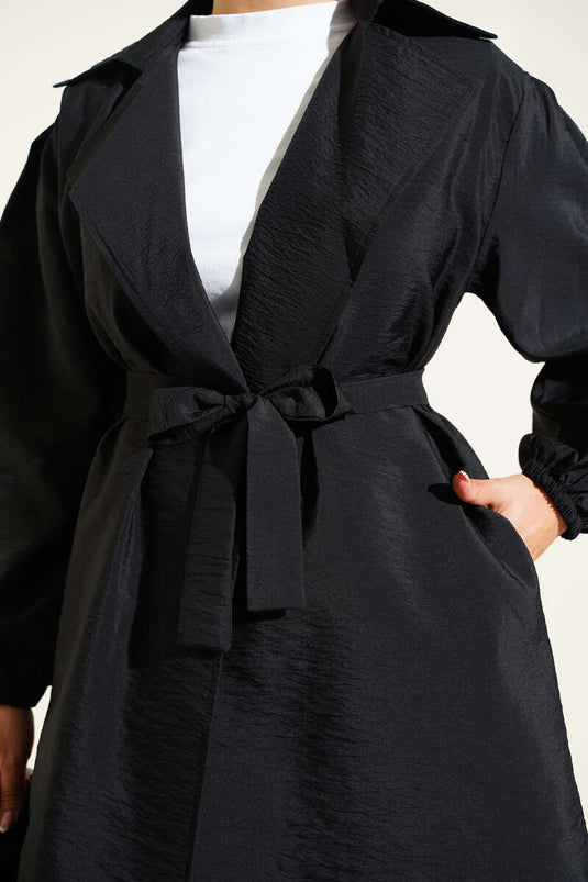 Trench-coat noir à double boutonnage, manches bouffantes et ceinture.