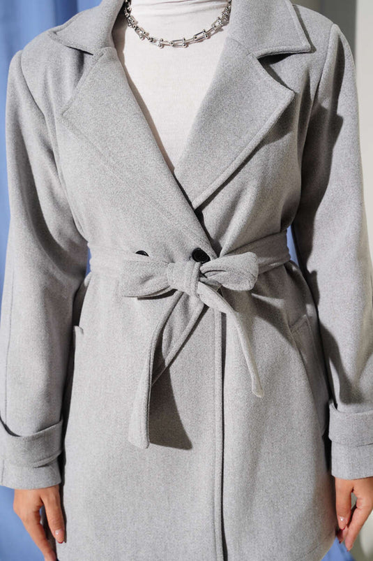 معطف قصير من الكشمير، رمادي اللون، بياقة مزدوجة الصدر وتفاصيل حزام.