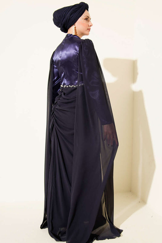 Marineblauwe avondjurk met schoudercape en details van steentjes.