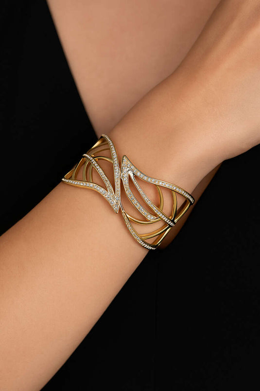 Gouden brede armband met bladmotief en steentjes.