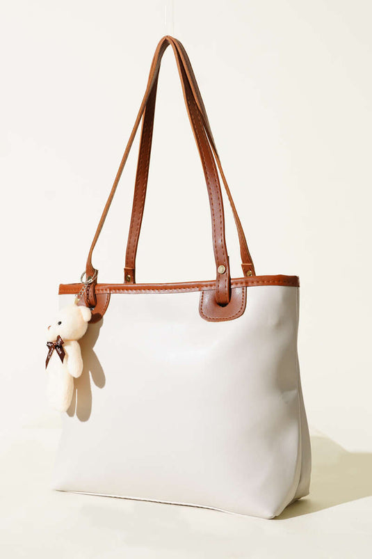 Grijze tas met dunne handgreep en teddybeeraccessoire.