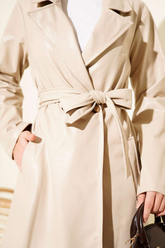 Trench-coat court en cuir beige, croisé et ceinturé.